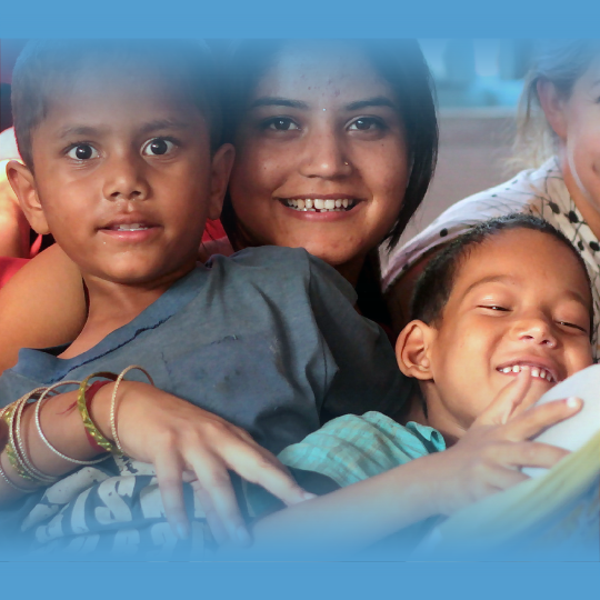 Children smiling at camera while one reads a book.